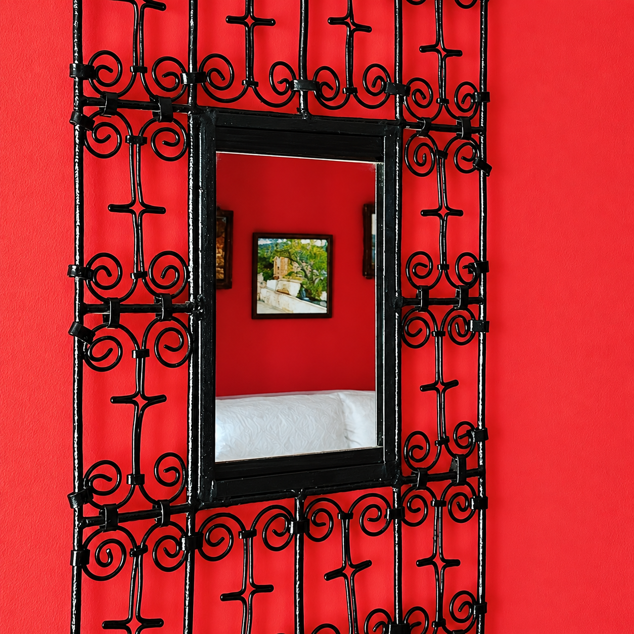Espejo decorativo con marco de forja negra sobre pared roja en el salón de Casa Rural Bekirent, en Bocairent.